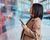 Young Asian businesswoman analysing and checking stock market over smartphone in downtown financial district. Stock exchange market trading board in background.