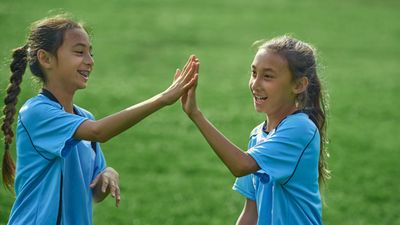 Kids Playing Soccer - two girls in blue t-shirts giving a high five.