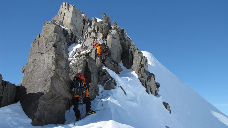 Researchers in orange jumpsuits climb a mountain peak.