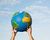 Hands holding a globe high in the air.